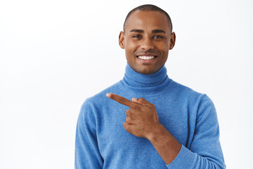 Close-up portrait of pleasant adult african american man showing way, pointing finger left and smiling friendly, customer recommend visit store, satisfied with good quality, white background