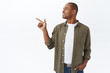 © Cookie Studio - Portrait of handsome adult african-american man in casual outfit, turn head and pointing finger left with pleased smile, picking from chart, showing good offer, making choice, white background