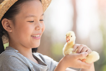 Poster - happy little girl with of small ducklings sitting outdoor. portrait of an adorable little girl, preschool or school age, happy child holding a fluffy baby gosling with both hands and smiling..