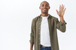 © Cookie Studio - Portrait of friendly african-american male in casual outfit, seeing person in crowd, attract friends attention, waving raised hand to say hi, informal greeting, smiling happy, white background