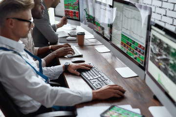 Wall Mural - Think about it. Achieve it. Three businessmen sitting at desktop front PC computers with financial graphs and statistics on monitors. Analysis of digital market and investment. Stock trade