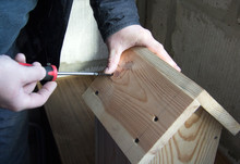 A Man With A Screwdriver Twists A Screw. He Makes By Hands A Wooden House For Birds