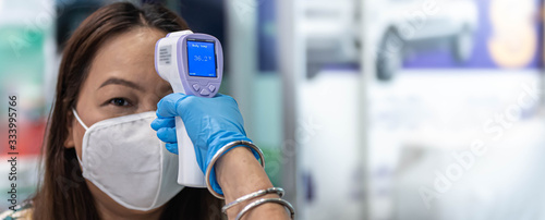 Cuadros en Lienzo CORONAVIRUS COVID-19 concept, Woman wearing mask with thermoscan or thermometer guns screening for coronavirus before allowed to go into a building