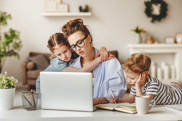 Small children being bored beside tired adult woman working on laptop at home