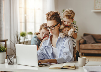 Wall Mural - Calm little children embracing serious adult woman using laptop together at home.