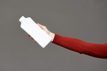 Wall Mural - White detergent bottle in female hand on gray background.