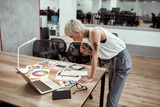 Fototapeta  - New project. Young stylish blonde tattooed female designer making some sketches and working with color swatch samples while standing near office desk