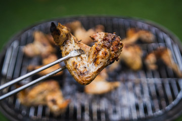 Grilling at summer weekend. Fresh meat preparing on grill. Lifting chicken wings with pair of tongs. Assorted delicious grilled meat.