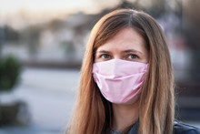 Young Woman With Pink Hand Made Cotton Face Nose Mouth Mask Portrait, Blurred Empty City Behind Her. Can Be Used During Coronavirus Covid-19 Outbreak Prevention