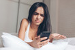 © Alexey Laputin - Young Annoyed angry woman looking on mobile phone in bed. Smiling Brunette Girl holding mobile phone
