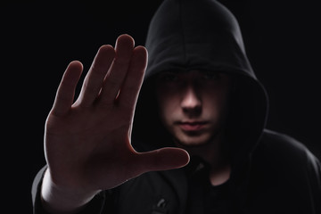 Wall Mural - A man in a black hood on a black background, studio photography. The idea of mysticism, mystery, crime and deception