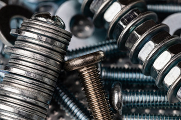 A Macro shot of the Threads of a small stainless steel bolt on a pile of washers, nuts and bolts.  Strong Contrast