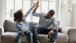© fizkes - African young father and daughter hold joysticks play playstation enjoy video games sit on couch, giving high five celebrating successful finish or start competition, activity with kids, fun concept