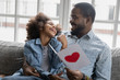 African loving daughter presented postcard with red heart to daddy, happy family sitting on sofa in living room reading wishes and laughing. Father Day celebration, life event congratulations concept