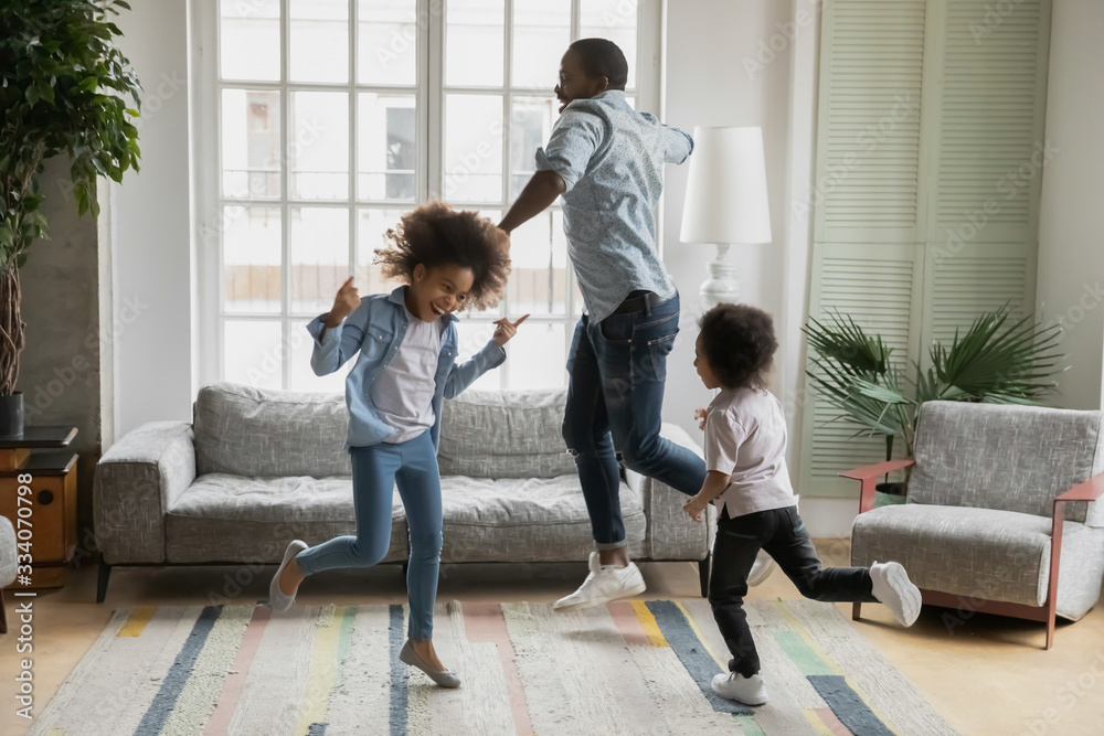 Active african funny dad little son and crazy daughter heavy metal or rock and roll lovers dancing in cozy living room relish life fooling around listening cool music scream with joy enjoy party hard - obrazy, fototapety, plakaty 