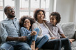 © fizkes - African couple with little kids enjoy communication telling jokes laughing resting on sofa. Concept of healthy happy family, first dwelling or new home, leisure weekend activities with children indoor