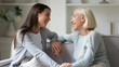 © fizkes - Smiling millennial girl and mature mother rest on couch in living room talking and laughing, happy elderly mom and adult grown-up daughter relax on sofa at home have pleasant conversation together