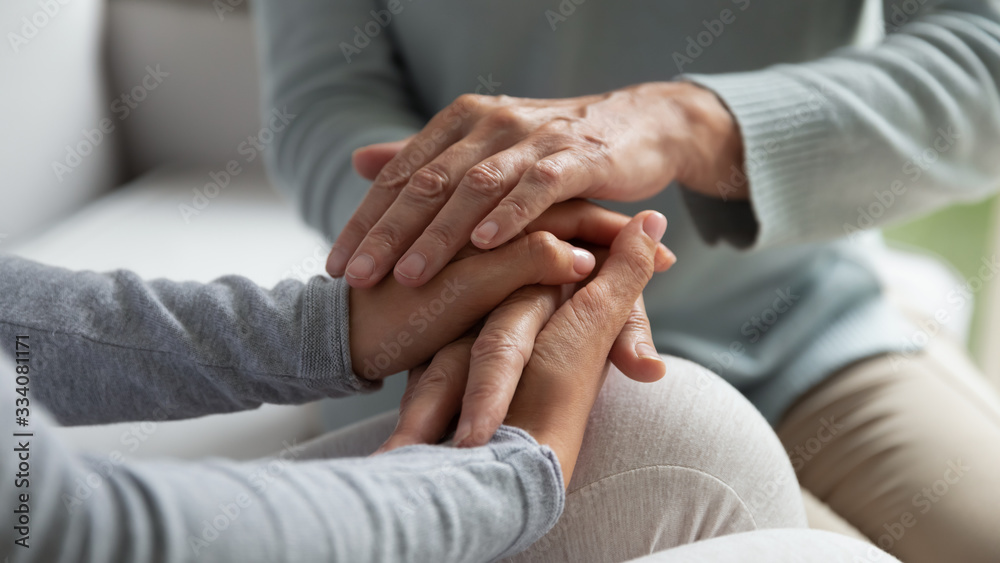 Close up of mature mother and grown-up daughter sit on couch holding hands share close intimate moment together, supportive caring elderly mom comfort adult girl child, show love and support - obrazy, fototapety, plakaty 
