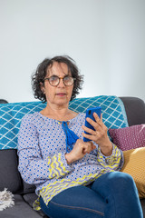 Sticker - cheerful brunette senior woman using smartphone while sitting on sofa