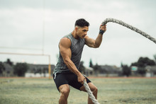Strong Man Exercising With Battle Ropes On A Field