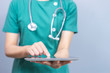 isolated close up body shot of female doctor holding a smart tablet device touching on the screen with her finger, representing technology in medical health care, wearing green scrub with stethoscope