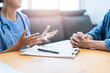 © Have a nice day  - Close up asian female doctor writing and filling forms and hand gesture of explaining on patients health care, with patients across with hands coupling in worry and stress. Within hospital office room