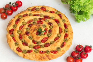 Sticker - Homemade italian flat bread - Focaccia contorta. With olives, olive oil, rosemary, tomatoes. Traditional recipe. Vegan. White concrete texture background.