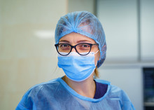 Doctor Or Nurse Smiling Behind Surgeon Mask. Closeup Portrait Of Young Woman Model In Blue Medical Scrub. Coronovirus Epidemic. Ambulance Station. Intensive Care Unit With Pneumonia Diagnosting. 