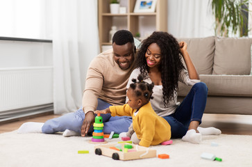 family, parenthood and people concept - happy african american mother, father and baby daughter playing with toy blocks at home