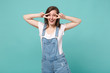 © ViDi Studio - Cheerful young brunette woman girl in casual denim clothes posing isolated on blue turquoise background studio portrait. People emotions lifestyle concept. Mock up copy space. Showing victory sign.