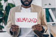 Cropped view of african american employee showing placard with unemployed lettering in office