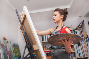 Wall Mural - Low angle shot of a beautiful woman enjoying painting at her workshop. Female painter drawing at art studio