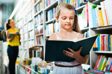 Wall Mural - Small girl in school age standing with open book