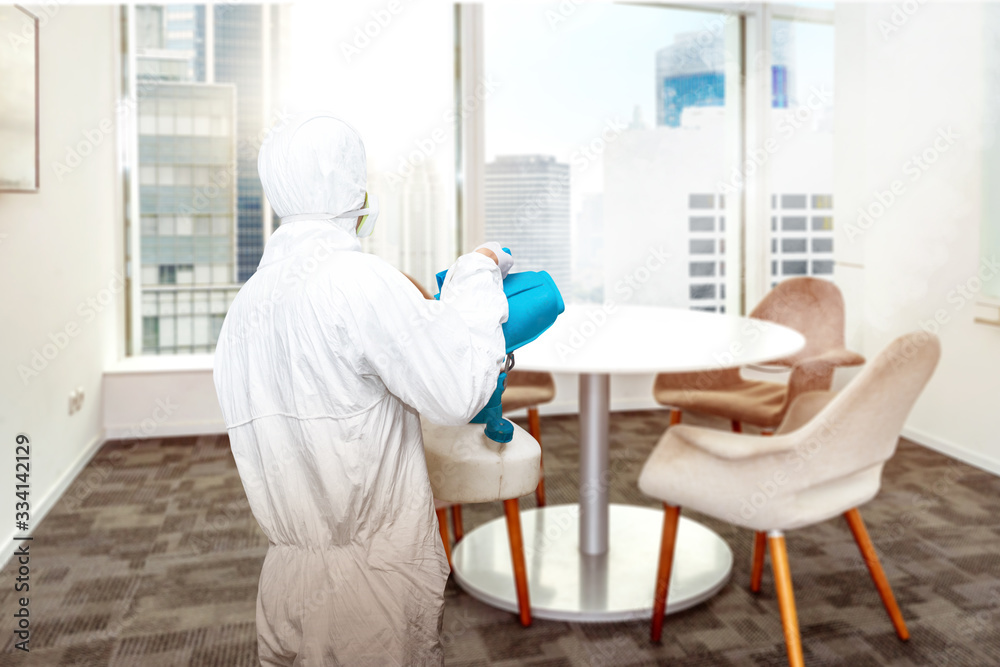 Man in a white protective suit spraying disinfectant in the office room - obrazy, fototapety, plakaty 