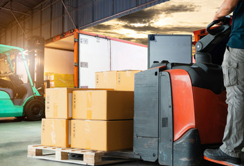 Wall Mural - Warehouse worker driving forklift pallet jack unloading pallet goods, package boxes, forklift loading shipment goods into a truck, road freight, warehouse industry delivery logistics and transport.