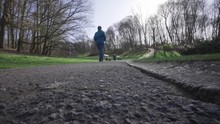 Man Drives A Witty Radio-controlled Car Behind Walking Woman In Beautiful Woluwepark In Wide Angle.
