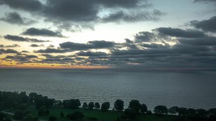 Wall Mural - aerial time lapse of rows of white fluffy cumulus clouds rolling over lake michigan as a bright oran