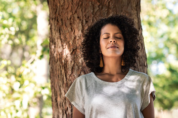 peaceful woman leaning against a tree with her eyes closed
