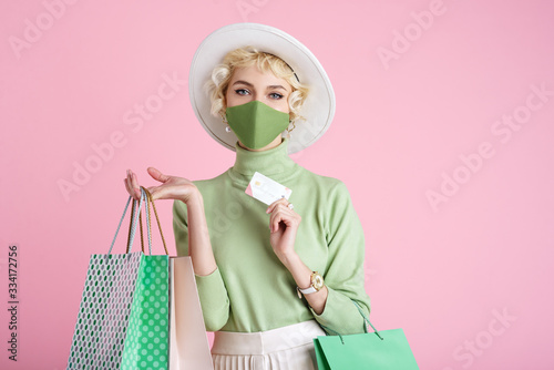 Fotomural Spring online shopping during quarantine conception: fashionable woman wearing protective mask posing with colorful paper bags and plastic bank card