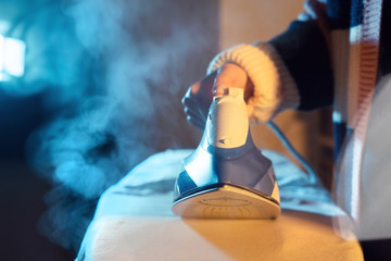 Close up on female caucasian hand woman holding steam iron ironing cloth dress in dark room at home in night or evening