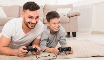 Cheerful dad and son playing video games at home