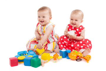 Two cute baby girls playing with toys, isolated on white. Having fun, smiling