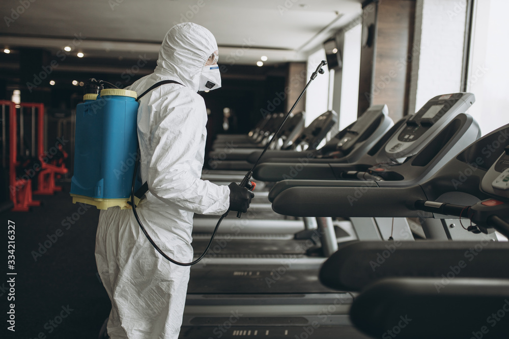 Cleaning and Disinfection in crowded places amid the coronavirus epidemic Gym cleaning and disinfection Infection prevention and control of epidemic. Protective suit and mask and spray bag - obrazy, fototapety, plakaty 