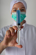 © coob.kz - Girl in a medical coat holds a large syringe with blue liquid - coronaviris vaccine