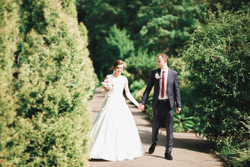 Stylish couple of happy newlyweds walking in the park on their wedding day with bouquet