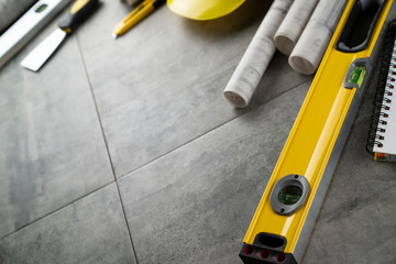 Contractor concept. Tool kit of the contractor: yellow hardhat, libella, hand saw, and notebook on the gray tiles background.