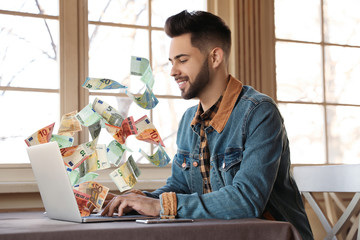 Wall Mural - Man with modern laptop and flying euro banknotes at table indoors. People make money online