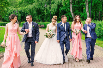 Wall Mural - Groom and bride walk with groomsman and bridesmaid in the park.