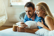 © Drazen - Happy couple using smart phone while relaxing on bed in the morning.
