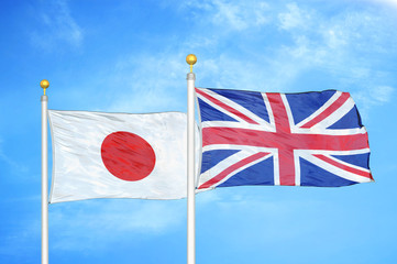 Japan and United Kingdom two flags on flagpoles and blue cloudy sky